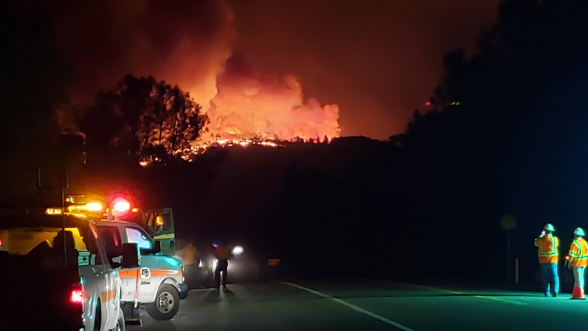 Highway crew working an evacuation route at night, fire visible on the ridge